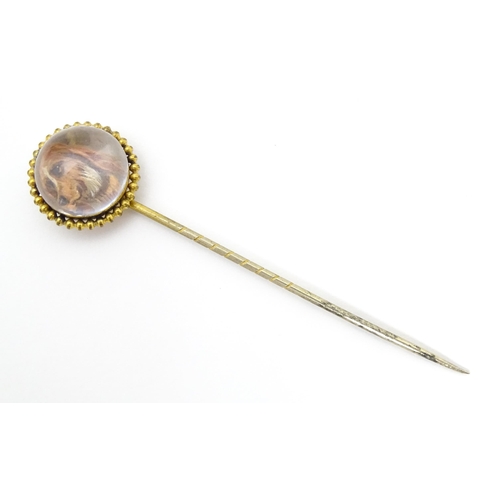 666 - A gilt metal stick pin surmounted by an Essex Crystal cabochon with dog head decoration. Cabochon ap... 