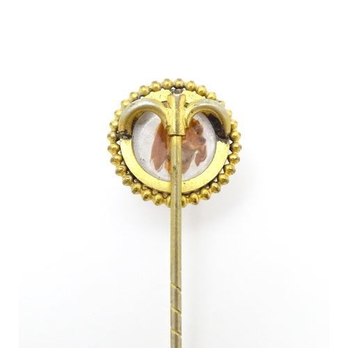 666 - A gilt metal stick pin surmounted by an Essex Crystal cabochon with dog head decoration. Cabochon ap... 