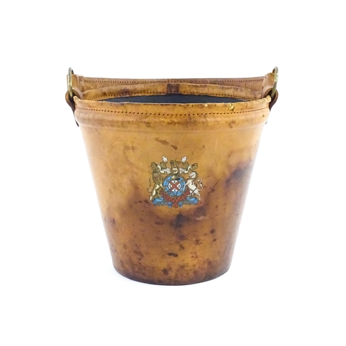 1149 - A 20thC leather covered fire bucket with swing handle and armorial / coat of arms detail. Approx. 11... 