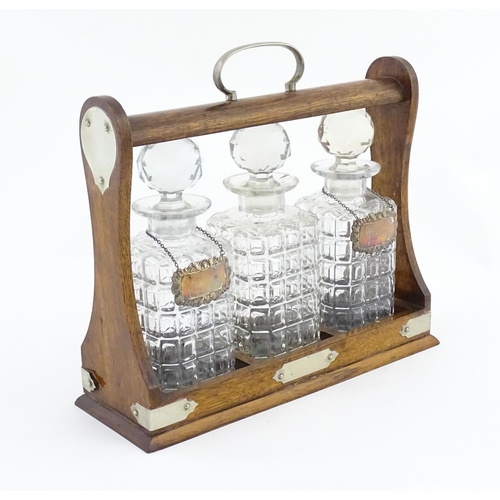 1204 - A late 19th / early 20thC oak tantalus with silver plate mounts, containing three glass decanters an... 