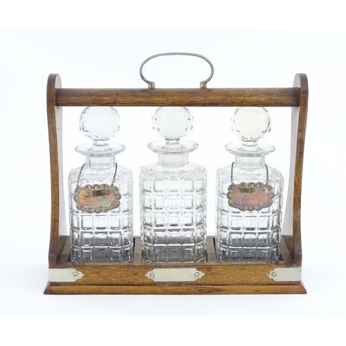 1204 - A late 19th / early 20thC oak tantalus with silver plate mounts, containing three glass decanters an... 