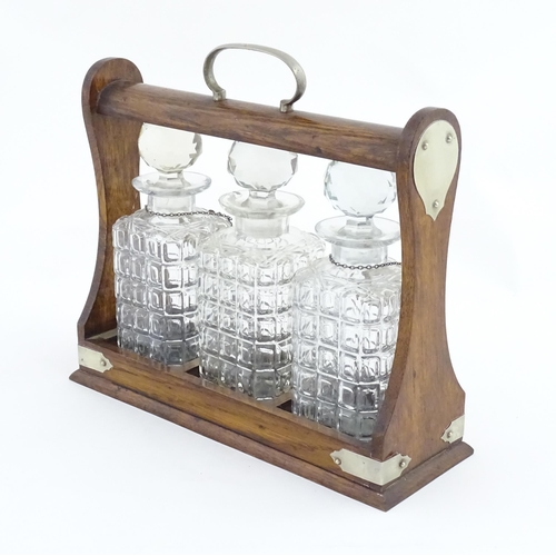 1204 - A late 19th / early 20thC oak tantalus with silver plate mounts, containing three glass decanters an... 