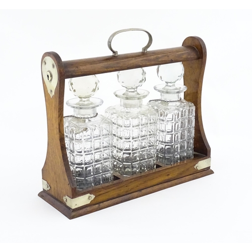 1204 - A late 19th / early 20thC oak tantalus with silver plate mounts, containing three glass decanters an... 