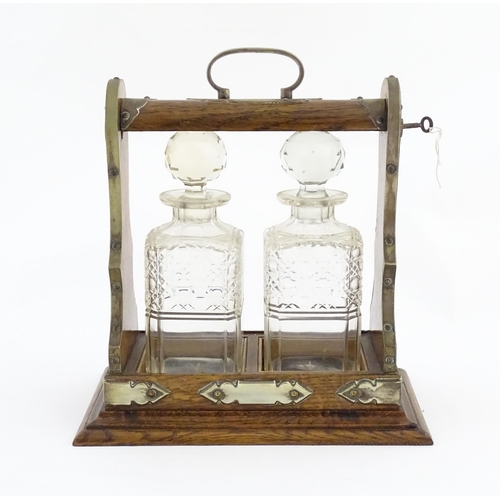 1245 - A late 19th / early 20thC oak tantalus with brass mounts and two glass decanters. Approx. 12 1/2