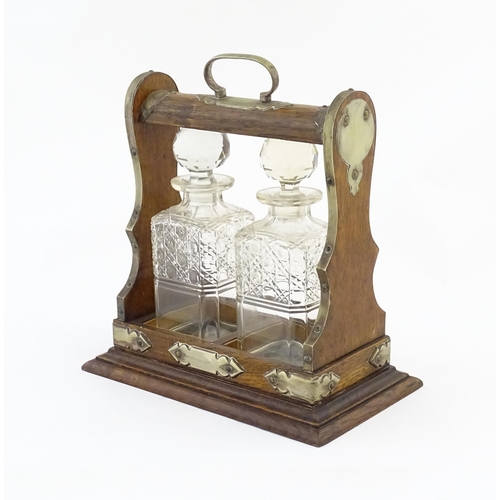 1245 - A late 19th / early 20thC oak tantalus with brass mounts and two glass decanters. Approx. 12 1/2