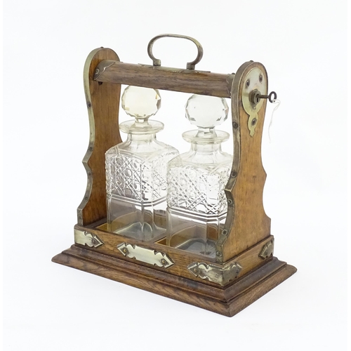 1245 - A late 19th / early 20thC oak tantalus with brass mounts and two glass decanters. Approx. 12 1/2