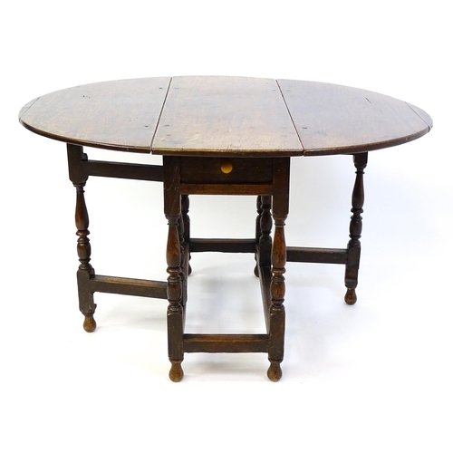 1332 - An early 18thC oak drop leaf table with a small drawer to end, the two leaves opening to form and ov... 