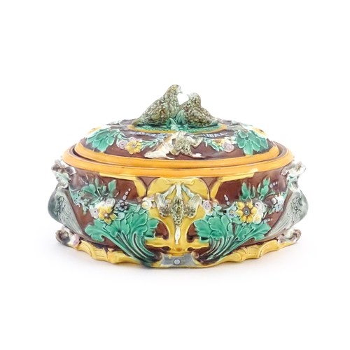 76 - A Victorian majolica game pie dish and cover, the body decorated in relief with birds, flowers and f... 