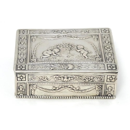 435 - A Continental silver box decorated with cherubs, floral and swag detail and opening to reveal a red ... 