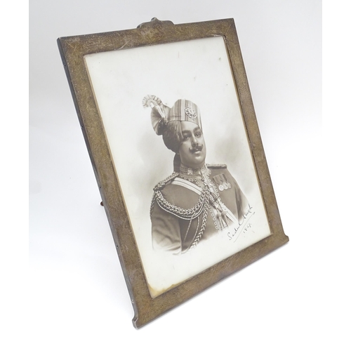 557 - A photograph frame with easel back  and  white metal surrounded with engraved decoration. Containing... 