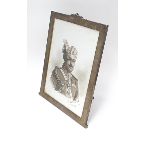 557 - A photograph frame with easel back  and  white metal surrounded with engraved decoration. Containing... 