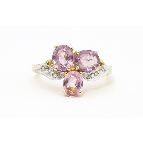 587 - A 10k gold ring set with diamonds and a trio of pink stones. Ring size approx. L