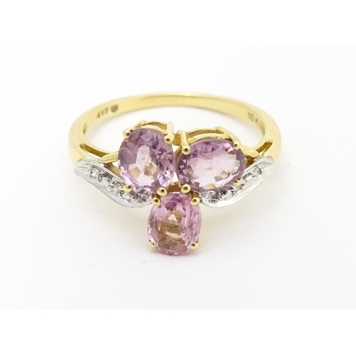 587 - A 10k gold ring set with diamonds and a trio of pink stones. Ring size approx. L