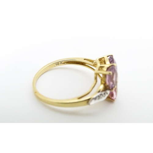 587 - A 10k gold ring set with diamonds and a trio of pink stones. Ring size approx. L