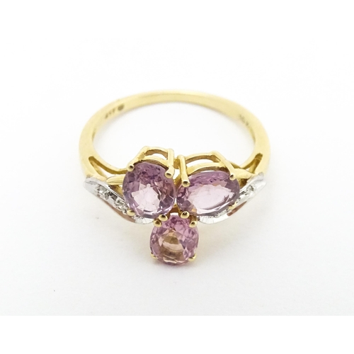 587 - A 10k gold ring set with diamonds and a trio of pink stones. Ring size approx. L