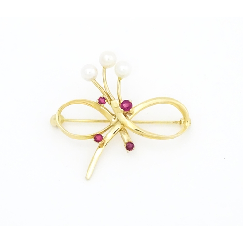 631 - A 10k gold brooch of bow form with pearl and ruby detail. Approx. 1 1/4