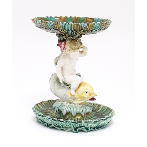 72 - A 19thC majolica tazza / centrepiece bowl, the figural stem with a cherub / putto riding a dolphin o... 