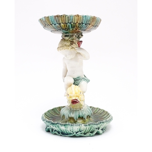 72 - A 19thC majolica tazza / centrepiece bowl, the figural stem with a cherub / putto riding a dolphin o... 