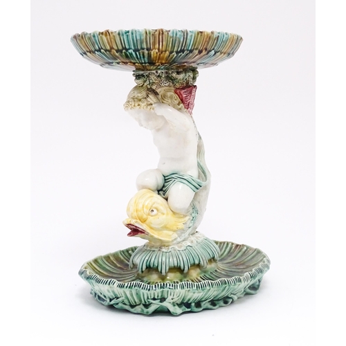 72 - A 19thC majolica tazza / centrepiece bowl, the figural stem with a cherub / putto riding a dolphin o... 