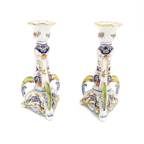 211 - A pair of French faience candlesticks with shaped bases, decorated with flowers and foliage. Marked ... 