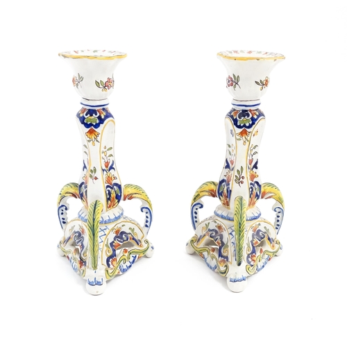 211 - A pair of French faience candlesticks with shaped bases, decorated with flowers and foliage. Marked ... 