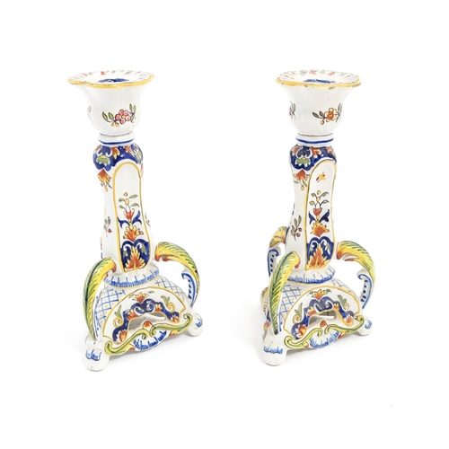 211 - A pair of French faience candlesticks with shaped bases, decorated with flowers and foliage. Marked ... 