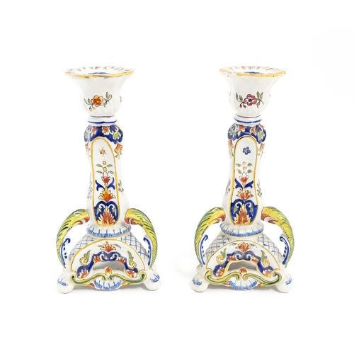 211 - A pair of French faience candlesticks with shaped bases, decorated with flowers and foliage. Marked ... 