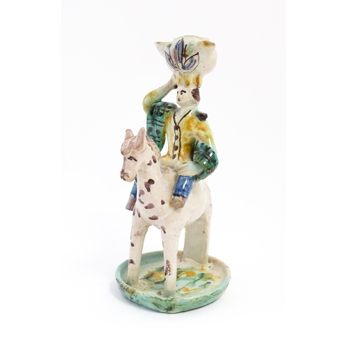 212 - A Continental faience style candlestick modelled as a figure on horseback carrying a vessel on his h... 