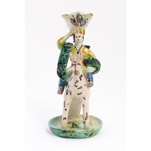 212 - A Continental faience style candlestick modelled as a figure on horseback carrying a vessel on his h... 