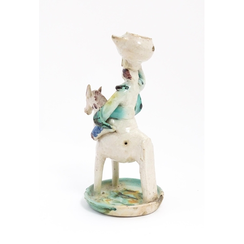 212 - A Continental faience style candlestick modelled as a figure on horseback carrying a vessel on his h... 