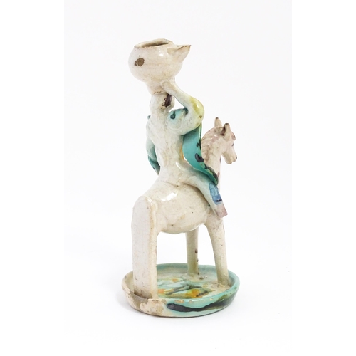 212 - A Continental faience style candlestick modelled as a figure on horseback carrying a vessel on his h... 