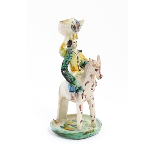 212 - A Continental faience style candlestick modelled as a figure on horseback carrying a vessel on his h... 