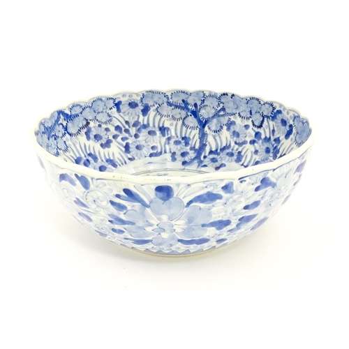 21 - A Japanese blue and white bowl with scalloped edge decorated with a central vase of flowers bordered... 