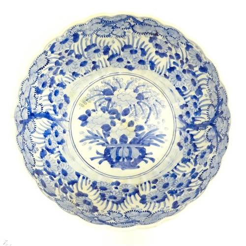 21 - A Japanese blue and white bowl with scalloped edge decorated with a central vase of flowers bordered... 