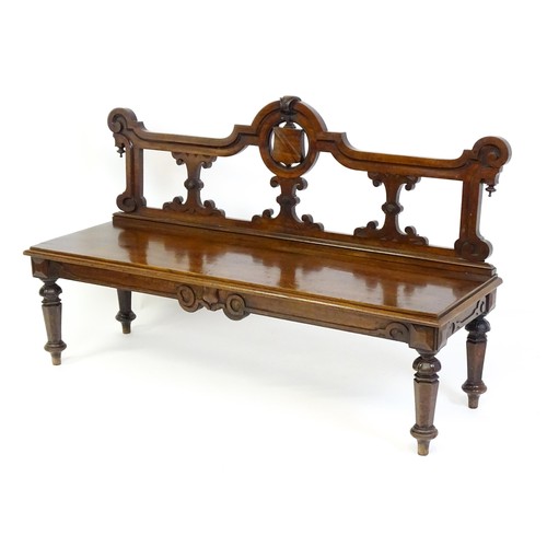 1439 - A Victorian mahogany bench, with a shaped top rail, carved terminals and an armorial shield to the c... 