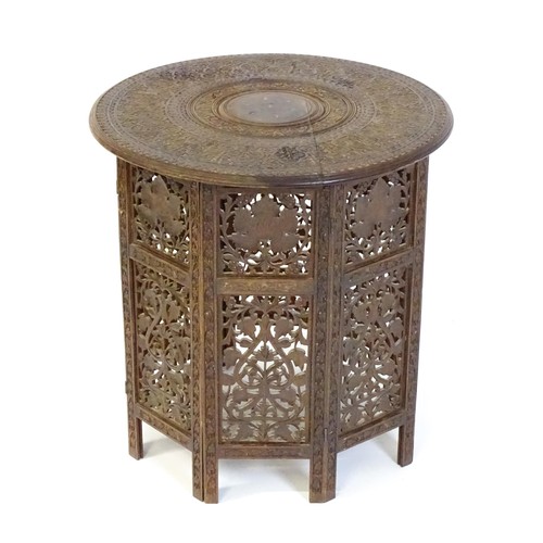 1474 - A late 19thC / early 20thC folding Islamic table with a floral carved top, brass inlay and the base ... 