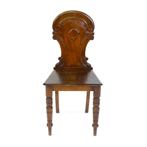 1497 - A Victorian mahogany hall chair with a carved backrest and raised on turned tapering front legs and ... 