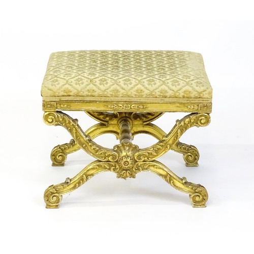 1509 - A late 19thC x-frame gilt stool, with a gesso and carved wood frame, the legs decorated with carved ... 