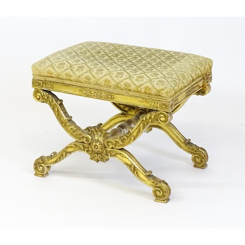 1509 - A late 19thC x-frame gilt stool, with a gesso and carved wood frame, the legs decorated with carved ... 