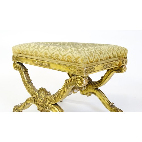 1509 - A late 19thC x-frame gilt stool, with a gesso and carved wood frame, the legs decorated with carved ... 