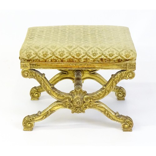 1509 - A late 19thC x-frame gilt stool, with a gesso and carved wood frame, the legs decorated with carved ... 