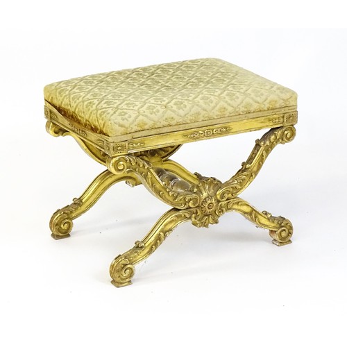 1509 - A late 19thC x-frame gilt stool, with a gesso and carved wood frame, the legs decorated with carved ... 