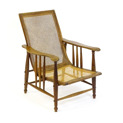 1560 - An Arts & Crafts bergère chair with a caned backrest and seat, the shaped arms supported by turned t... 