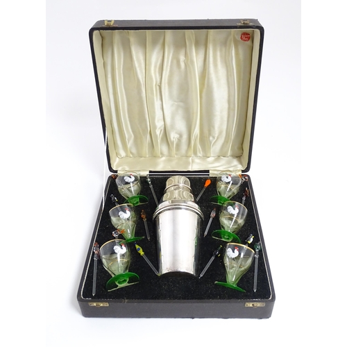 1145 - A cased Art Deco cocktail set comprising a silver plate cocktail shaker with six green footed glasse... 