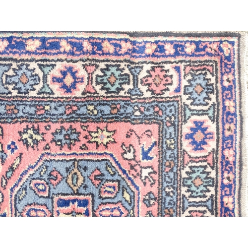 1343 - Carpet / Rug : A salmon pink ground rug with geometric and floral motifs and borders worked in blue ... 