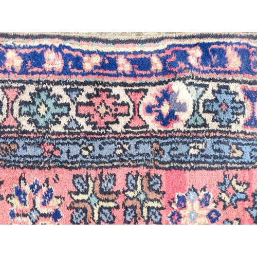 1343 - Carpet / Rug : A salmon pink ground rug with geometric and floral motifs and borders worked in blue ... 