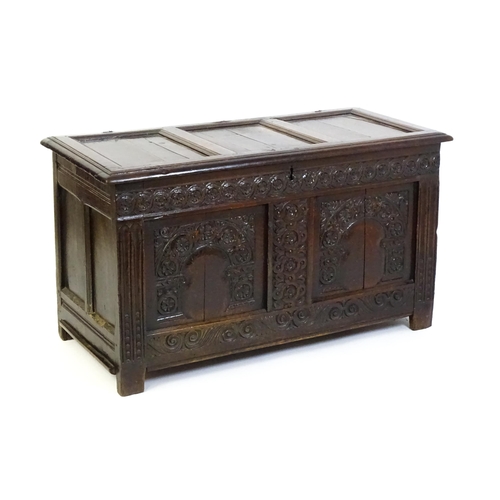 1456 - A late 17thC oak coffer with a three panel lid above a floral wave and scroll carved front, the coff... 