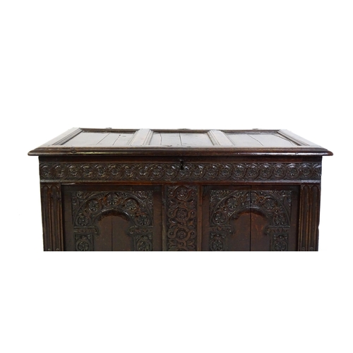 1456 - A late 17thC oak coffer with a three panel lid above a floral wave and scroll carved front, the coff... 