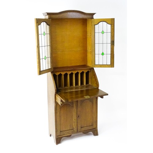 115 - An early / mid 20thC glazed oak bureau, with an arched pediment above stained, leaded glass doors, a... 