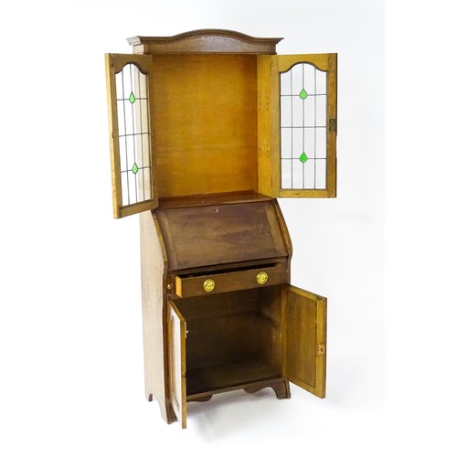 115 - An early / mid 20thC glazed oak bureau, with an arched pediment above stained, leaded glass doors, a... 